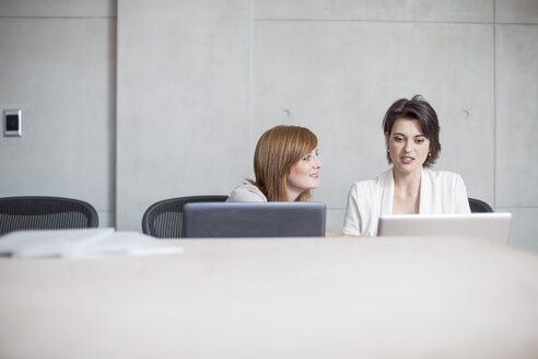 Zwei Geschäftsfrauen benutzen Laptops in einem Konferenzraum - ZEF003043