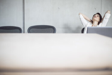 Businesswoman with laptop in conference room leaning back - ZEF003049