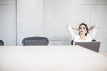 Businesswoman with laptop in conference room leaning back - ZEF003095