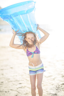Mädchen am Strand lächelnd und hält eine Luftmatratze - ZEF003304
