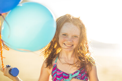 Mädchen am Strand lächelnd und hält Luftballons - ZEF003309