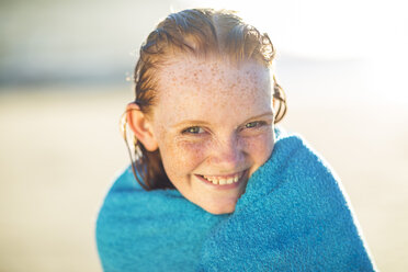 Porträt eines lächelnden Mädchens am Strand, eingewickelt in ein Strandtuch - ZEF003310