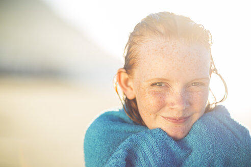 Porträt eines lächelnden Mädchens am Strand, eingewickelt in ein Strandtuch - ZEF003311