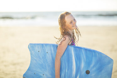 Mädchen am Strand lächelnd und hält ein Boogie Board - ZEF003316