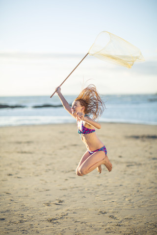 Glückliches Mädchen am Strand, das mit einem Schmetterlingsnetz springt, lizenzfreies Stockfoto