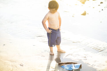 Boy on the beach playing with a toy wooden boat in the water - ZEF003416