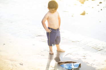 Junge am Strand, der mit einem Spielzeug-Holzboot im Wasser spielt - ZEF003416