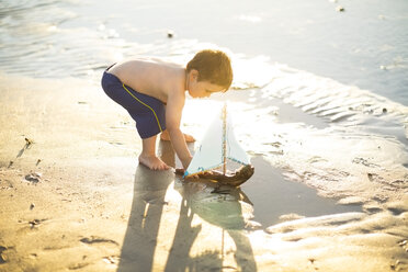 Boy on the beach playing with a toy wooden boat in the water - ZEF003428
