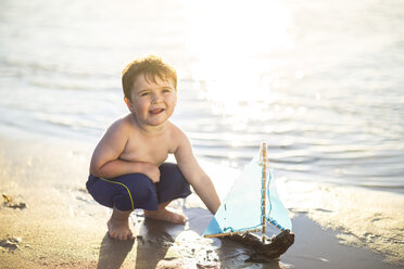 Junge am Strand, der mit einem Spielzeug-Holzboot im Wasser spielt - ZEF003418