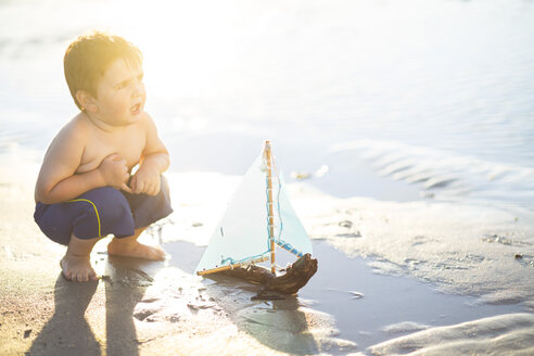 Junge am Strand, der mit einem Spielzeug-Holzboot im Wasser spielt - ZEF003419