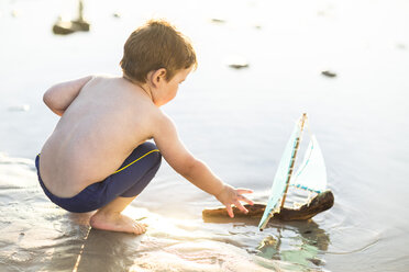 Junge am Strand, der mit einem Spielzeug-Holzboot im Wasser spielt - ZEF003420