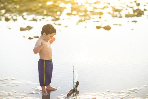 Junge spielt mit einem Spielzeug-Holzboot im Wasser, lizenzfreies Stockfoto