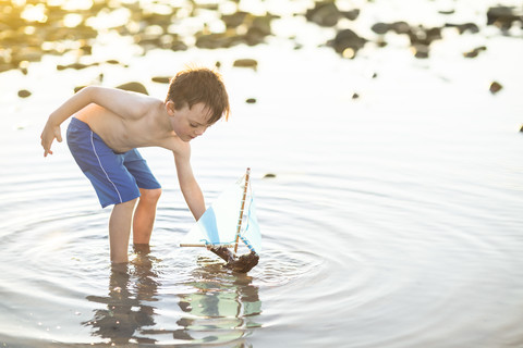 Junge spielt mit einem Spielzeug-Holzboot im Wasser, lizenzfreies Stockfoto