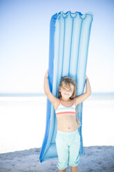 Lächelndes Mädchen am Strand, das eine Luftmatratze hält - ZEF003337