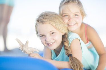 Two smiling girls on beach lying on a lilo with a starfish - ZEF003349