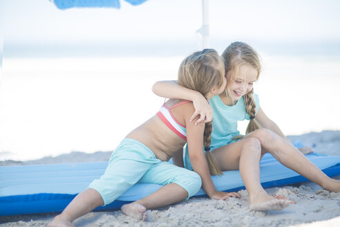 Zwei glückliche Mädchen am Strand auf einer Luftmatratze sitzend - ZEF003352