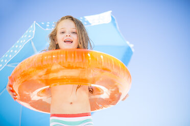 Smiling girl on beach holding an orange floating tyre - ZEF003356