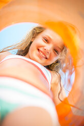 Smiling girl on beach holding an orange floating tyre - ZEF003359