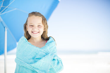Lächelndes Mädchen am Strand, eingewickelt in ein Handtuch - ZEF003364