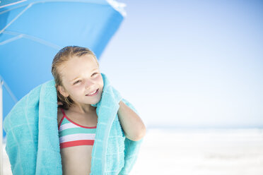 Smiling girl on beach drying off with a beach towel - ZEF003365