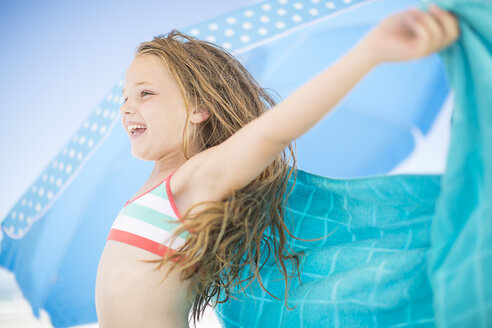 Smiling girl on beach drying off with a beach towel - ZEF003367