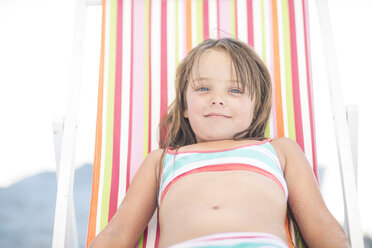 Lächelndes Mädchen am Strand, das sich auf einem Liegestuhl entspannt - ZEF003388