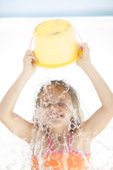 Girl on beach splashing herself with a bucket of water - ZEF003398