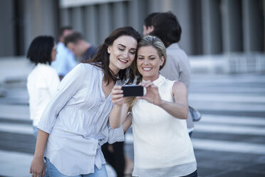 Zwei lächelnde Frauen in der Stadt, die ein Mobiltelefon halten - ZEF003255