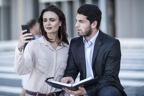 Geschäftsmann und Frau mit Tagebuch und Mobiltelefon in der Stadt, lizenzfreies Stockfoto