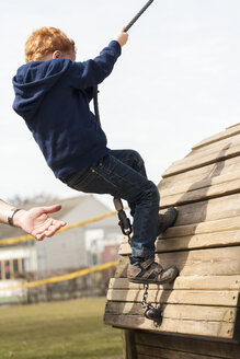 Junge auf Spielplatz mit helfender Hand an seiner Seite - NNF000358