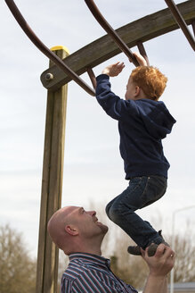 Vater hilft seinem Sohn auf dem Spielplatz beim Klettern auf dem Klettergerüst - NNF000309