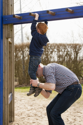 Vater hilft seinem Sohn auf dem Spielplatz beim Klettern auf dem Klettergerüst, lizenzfreies Stockfoto