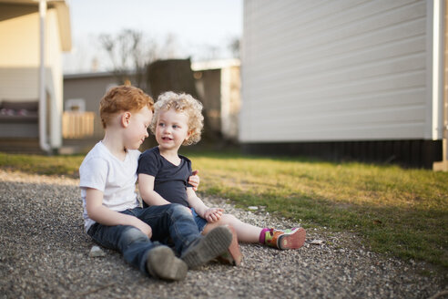Kleines Mädchen und Junge sitzen auf einem Kiesweg - NNF000359