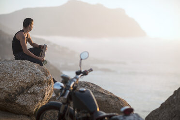 South Africa, Cape Town, motorcyclist sitting on rock at the coast enjoying view - ZEF003609