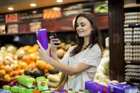 Woman at supermarket scanning prices with her smart phone - ZEF004183