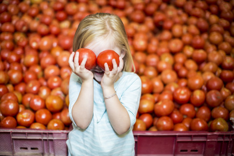 Kleines Mädchen vor einem Tomatenstand, das sich die Augen mit Tomaten bedeckt, lizenzfreies Stockfoto