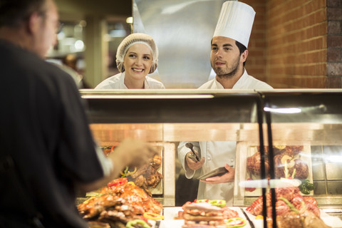 Male chef and assistant helping clients at food display stock photo