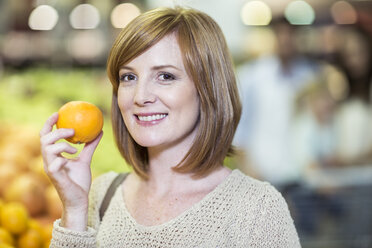 Young woman in supermarket holding orange - ZEF004208