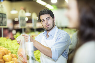 Shop assistant helping client choosing oranges - ZEF004209