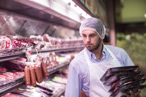 Butcher filling shelf with packaged meat stock photo