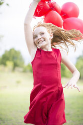 Portrait of running girl with red balloons wearing red dress - ZEF004390