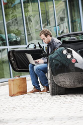 Young man with sitting in his sports car using laptop - HHF005023