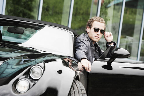 Junger Mann mit Sonnenbrille sitzt in einem schwarzen Sportwagen - HHF005021