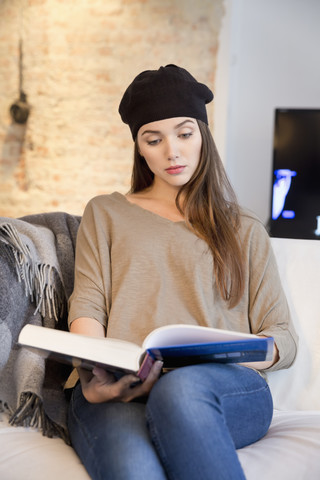 Junge Frau auf dem Sofa beim Lesen eines Bildbandes, lizenzfreies Stockfoto