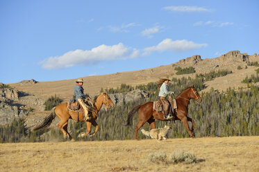 USA, Wyoming, zwei reitende Cowgirls und ihr laufender Hund - RUEF001374