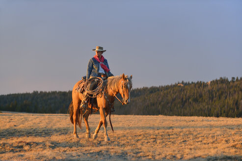 USA, Wyoming, Cowgirl reitet im Abendlicht - RUEF001406