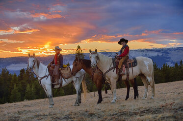 USA, Wyoming, zwei junge Cowboys sitzen bei Sonnenuntergang auf ihren Pferden - RUEF001419