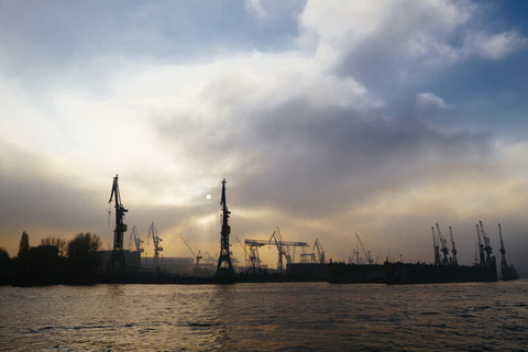 Deutschland, Hamburg, Hafenkräne an der Elbe am Abend, lizenzfreies Stockfoto