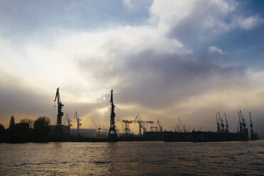 Deutschland, Hamburg, Hafenkräne an der Elbe am Abend - KRPF001217