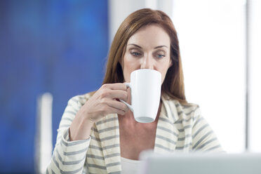 Geschäftsfrau im Büro trinkt Kaffee und arbeitet am Laptop - ZEF003105